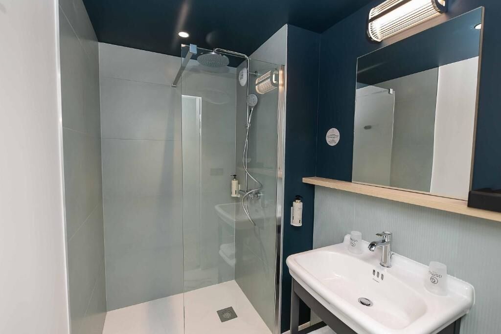 A modern bathroom with a glass-enclosed shower, a white sink with two faucets, and a mirror above the sink.