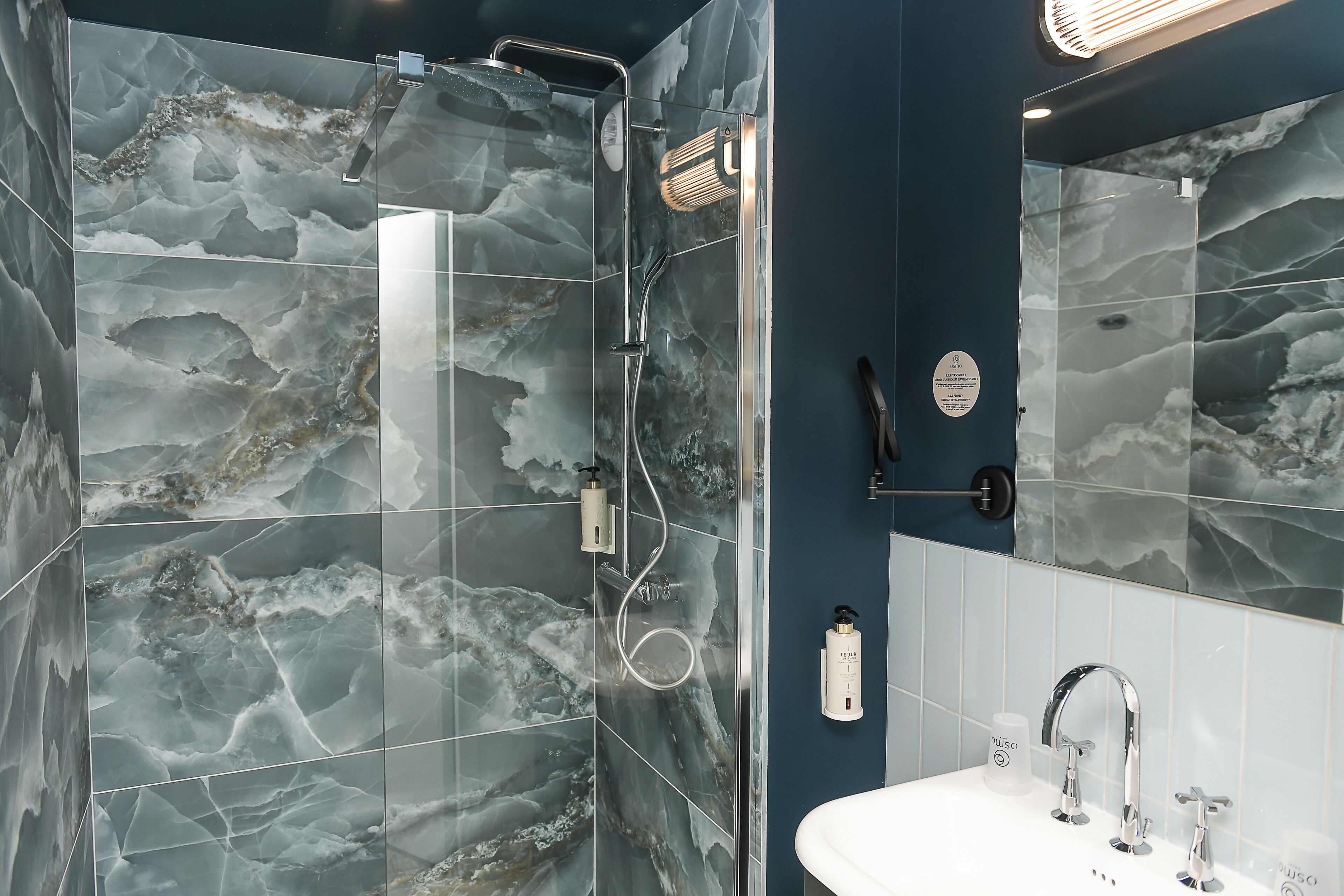 Une salle de bain moderne avec une douche à parois de verre, un lavabo blanc doté de robinetterie chromée et des murs à motifs de marbre.