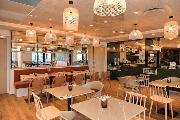 A restaurant interior with multiple dining tables and chairs, hanging light fixtures, and a counter area.