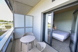 A balcony with a table and chairs, a bed, and a sliding glass door leading to a bedroom.