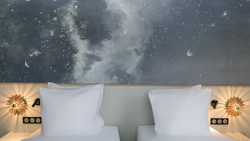 A hotel room with a bed, two bedside tables, and a wall mural of a starry sky.
