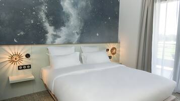 Habitación de hotel con cama, un mural del cielo nocturno, un aplique de pared y una ventana con cortinas.