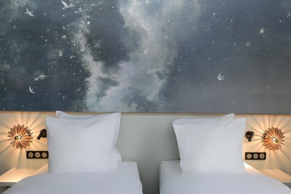 A hotel room with two beds, a starry night mural on the wall, and wall-mounted lamps.