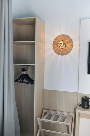 Ein Hotelzimmer mit einem Holzschrank, einer Wandleuchte, einem Kleiderständer und einer kleinen Holzbank.