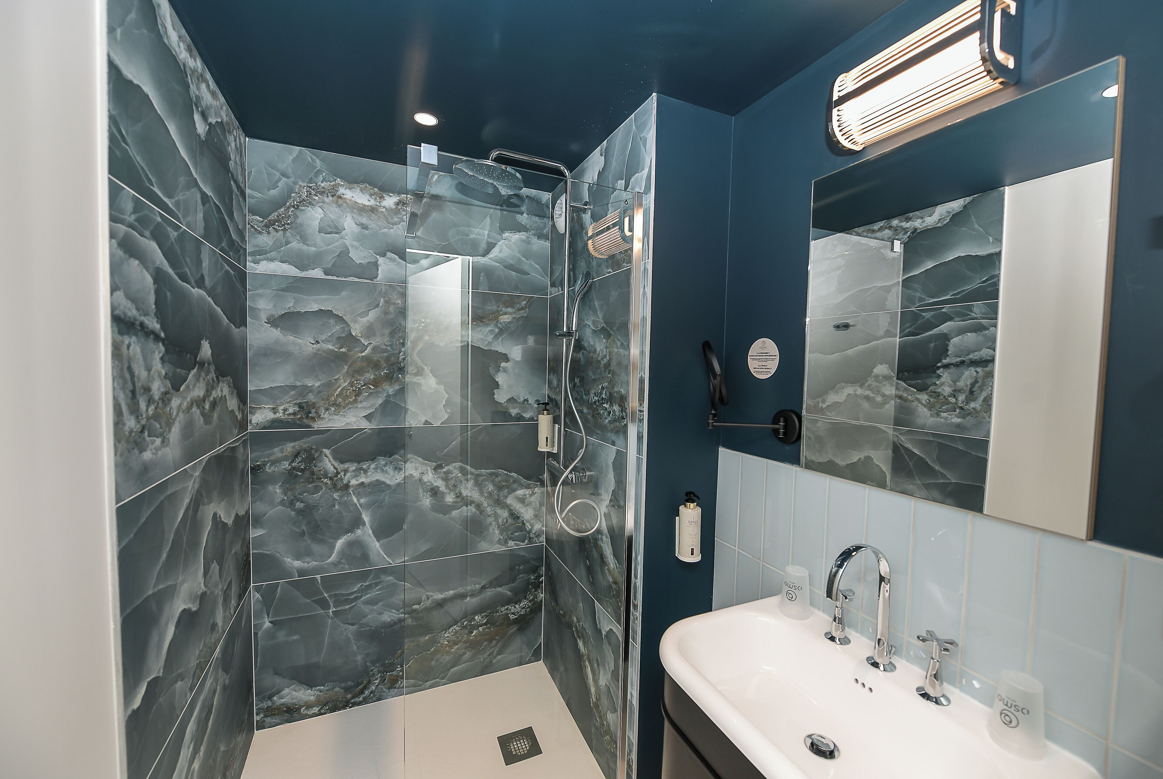 Un baño moderno con ducha de vidrio, un espejo grande y un lavamanos blanco.