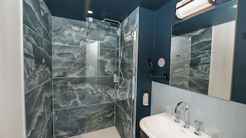 Un baño moderno con ducha de vidrio, un espejo grande y un lavamanos blanco.