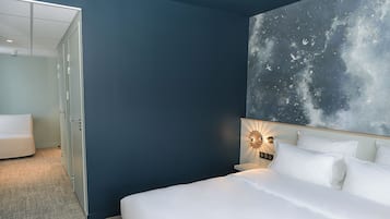A hotel room with a bed, a nightstand, a wall-mounted light, and a door leading to another room.