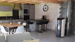 A modern kitchen with a wooden ceiling, a large clock, and a stone wall.
