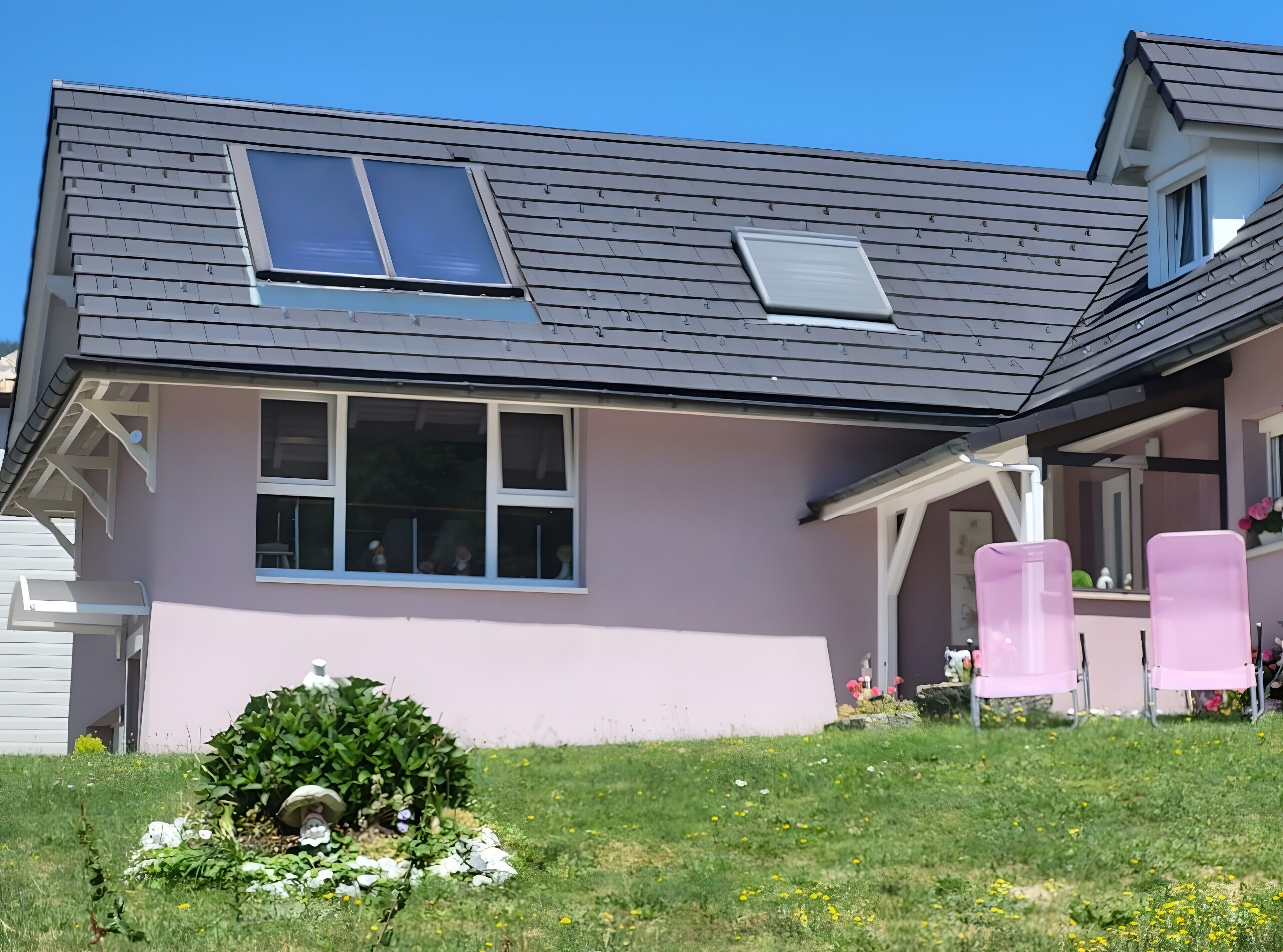Une maison avec un toit en pente, une grande fenêtre et un petit porche avec des chaises roses.