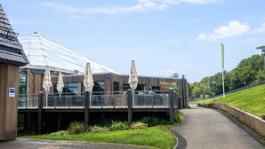 A modern building with a glass structure, outdoor seating with umbrellas, and a pathway leading to it. - 6 Person Holiday Park Home in Dienstweiler (Oberhambach)