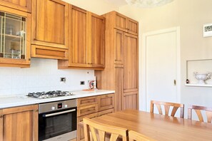 A kitchen with wooden cabinets, a gas stove, an oven, and a dining table with chairs. - SE234 – Senigallia, three-room apartment in the center with terrace and air conditioning (Senigallia)
