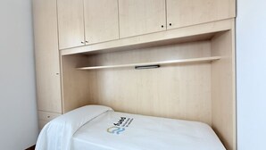 Een kleine kamer met een enkel bed, een houten kast, een nachtkastje en een bed met een wit laken.