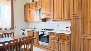 Een keuken met houten kastjes, een fornuis, een wasmachine en een eettafel met stoelen.