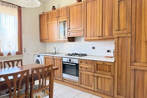 A kitchen with wooden cabinets, a stove, a washing machine, and a dining table with chairs. - SE234 – Senigallia, three-room apartment in the center with terrace and air conditioning (Senigallia)