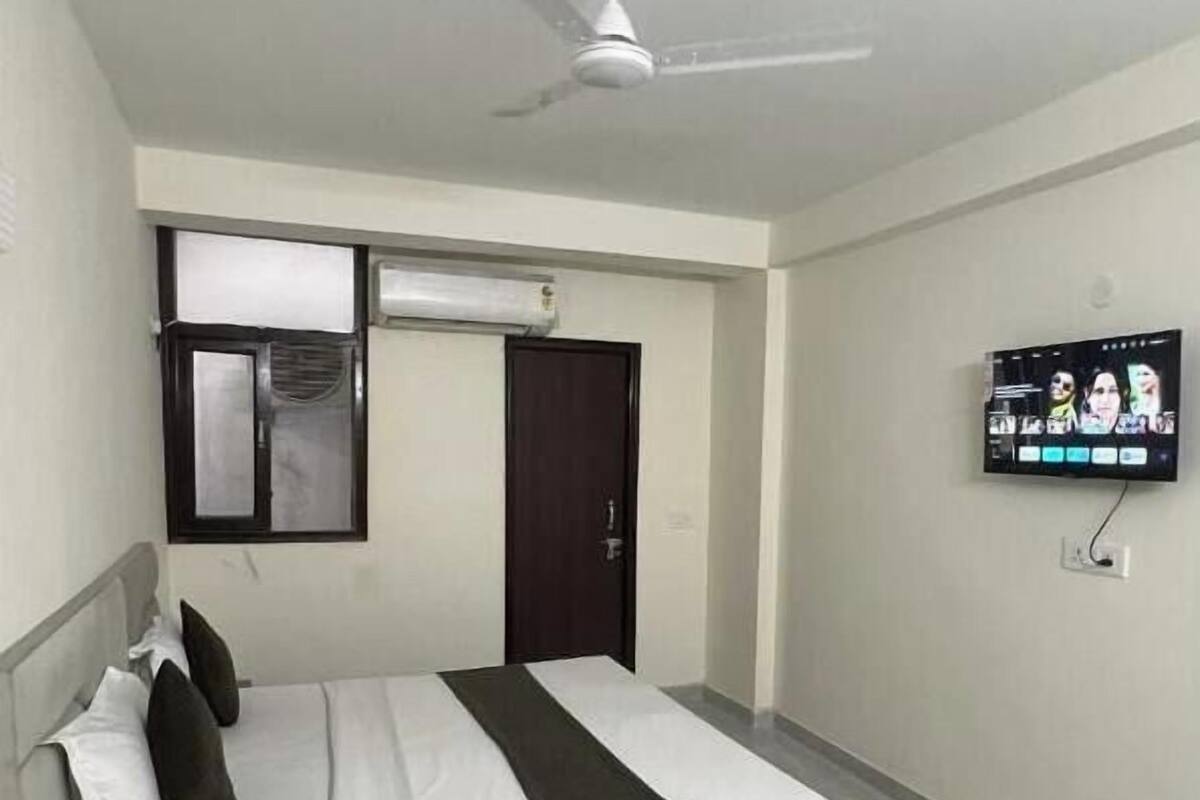 Una habitació d'hotel amb un llit, un ventilador de sostre, un aparell d'aire condicionat, un televisor penjat a la paret i una porta.