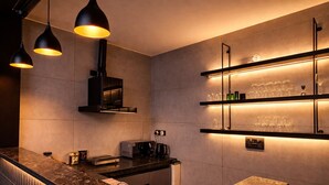 A modern kitchen with a marble countertop, black pendant lights, a built-in oven, and glassware on shelves. - The Luxury Penthouse (New Delhi)