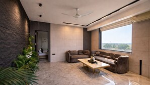 A modern living room with a sectional sofa, a coffee table, and a large window offering a view. - The Luxury Penthouse (New Delhi)