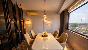 A modern dining area with a marble table, cushioned chairs, pendant lighting, and a view of the city through large windows. - The Luxury Penthouse (New Delhi)