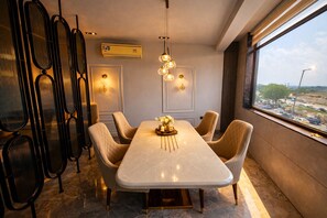 A modern dining area with a marble table, cushioned chairs, pendant lighting, and a view of the city through large windows. - The Luxury Penthouse IGI Airport Delhi (New Delhi)