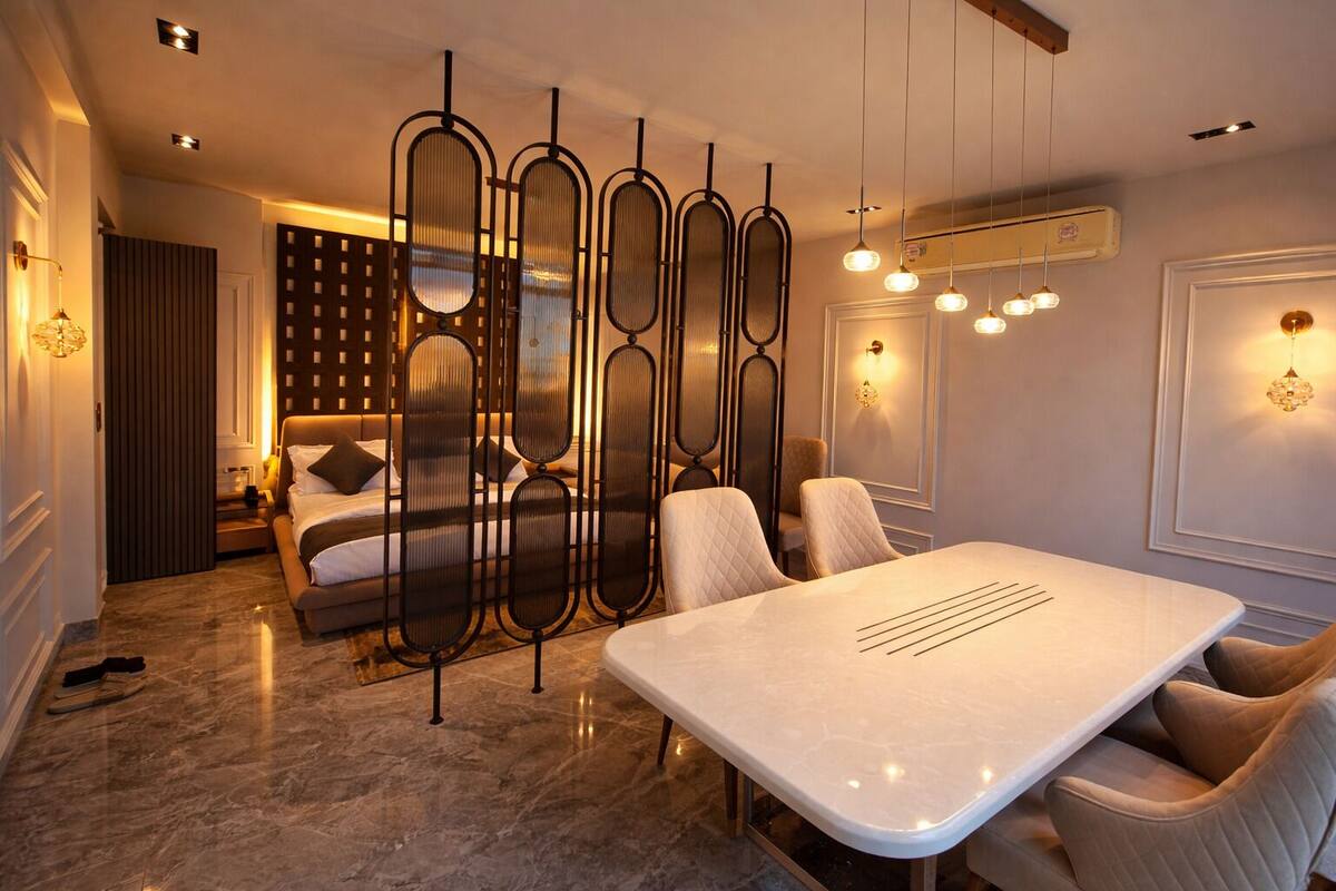 A modern hotel room with a bed, a dining table, and a seating area.