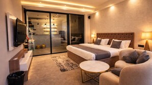 A modern hotel room with a large bed, a sofa, a small round table, and a TV mounted on the wall. - The Luxury Penthouse (New Delhi)