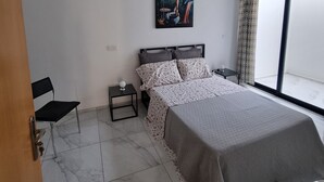 A bedroom with a bed, a chair, a nightstand, a painting, and a large window. - Explore the City from this Modern Loft (Praia)