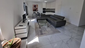 A modern living room with a sectional sofa, a flat-screen TV, a dining area, and a kitchen with white cabinets. - Explore the City from this Modern Loft (Praia)