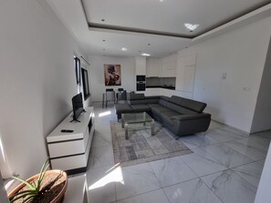 A modern living room with a sectional sofa, a flat-screen TV, a dining area, and a kitchen with white cabinets. - Explore the City from this Modern Loft (Praia)
