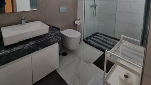 A modern bathroom with a large mirror, a sink, a toilet, a shower, and a small shelf with a roll of toilet paper. - Explore the City from this Modern Loft (Praia)