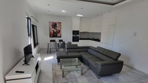 A modern living room with a sectional sofa, a glass coffee table, and a TV on a white console. - Explore the City from this Modern Loft (Praia)