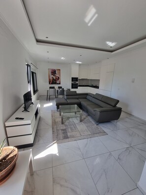 A modern living room with a sectional sofa, a glass coffee table, and a TV on a white console. - Explore the City from this Modern Loft (Praia)