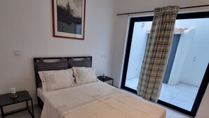 A bedroom with a bed, a nightstand, a framed picture, and a large window with a curtain. - Explore the City from this Modern Loft (Praia)