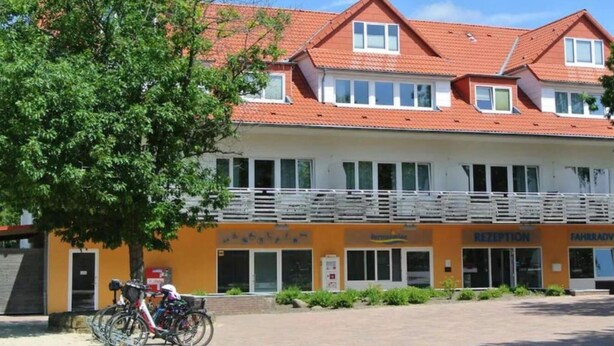 Un edificio a due piani con tetto in tegole rosse, una reception e un’area per il parcheggio delle biciclette.