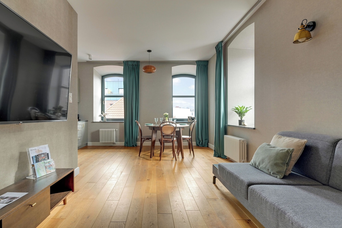 Un salon moderne comprenant un coin repas, un plancher en bois, un canapé gris et un téléviseur fixé au mur.