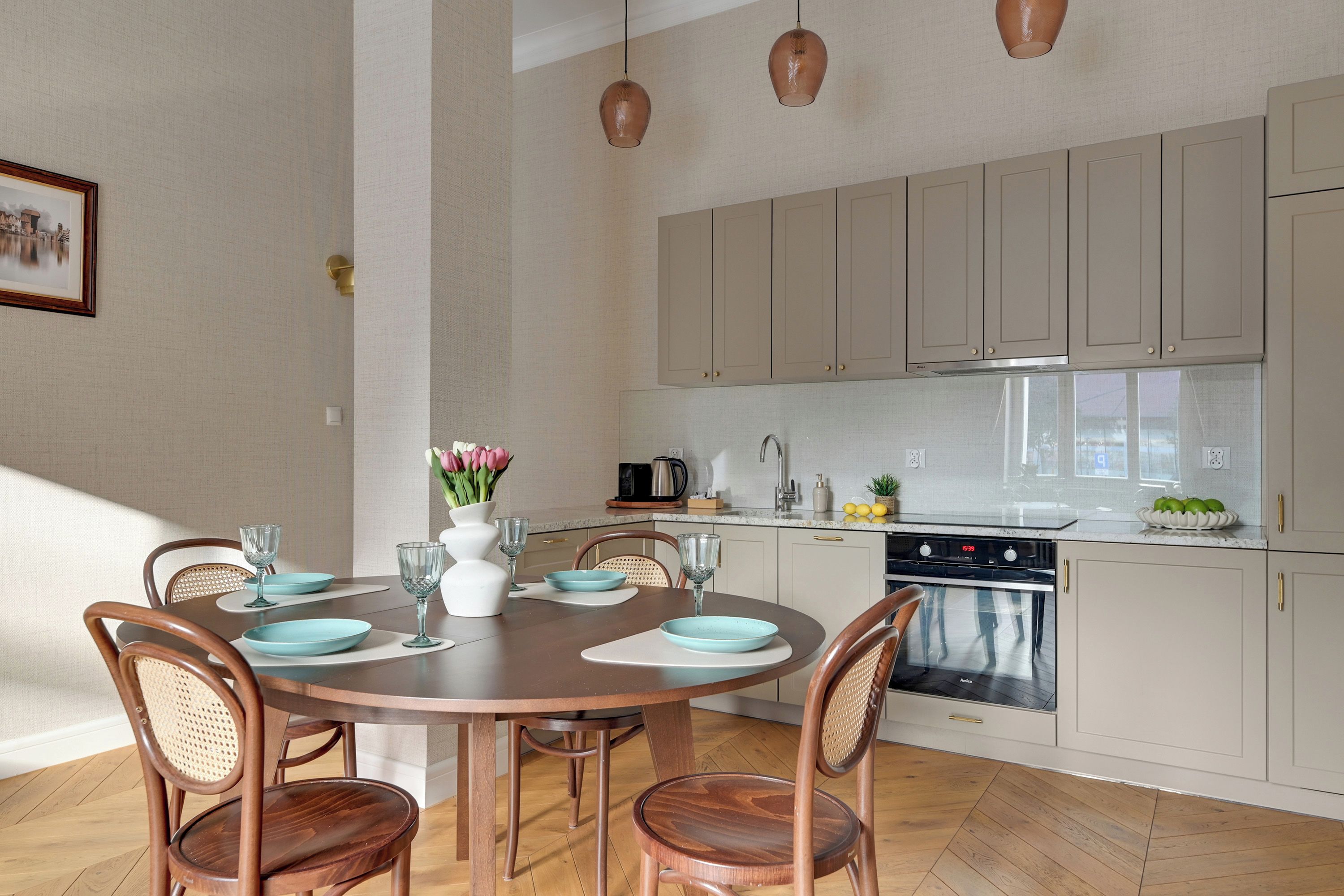 A modern kitchen with white cabinets, a dining table with chairs, and pendant lights.