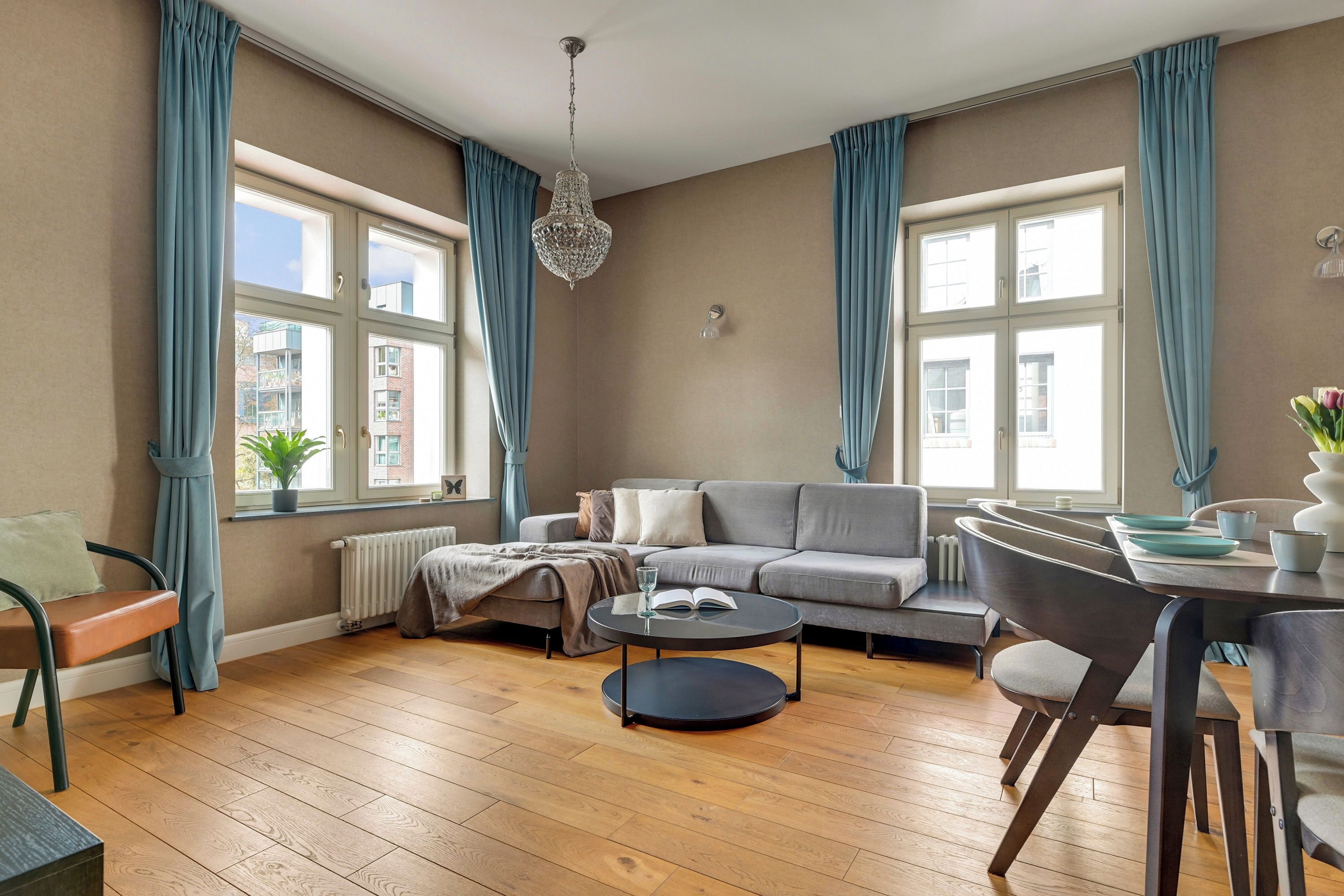 Een moderne woonkamer met een grijze bank, een ronde salontafel en een eethoek met een tafel en stoelen.