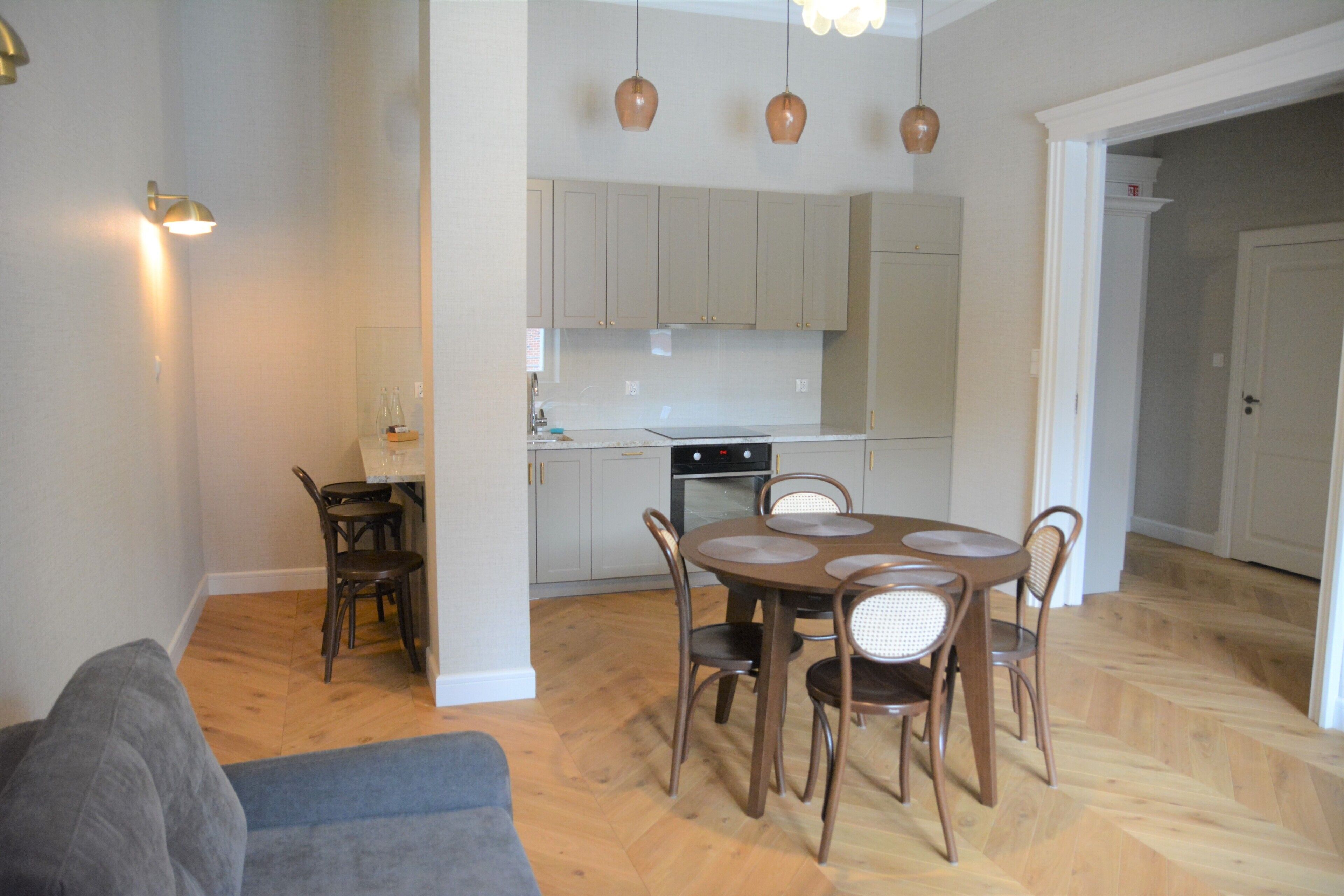 A compact kitchen with a dining area, a sofa, and a staircase leading to another room.