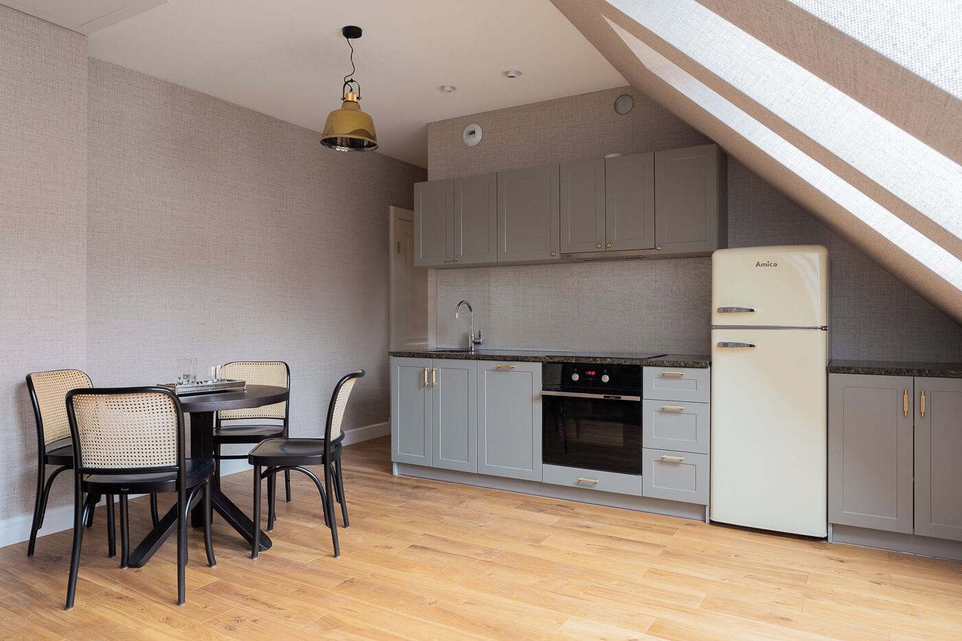 A compact kitchen with grey cabinets, a white refrigerator, and a dining area with a table and chairs.