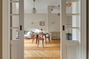 Une porte ouverte donne sur un espace repas doté d’un parquet en bois disposé en point de Hongrie, d’une table ronde et de deux chaises.