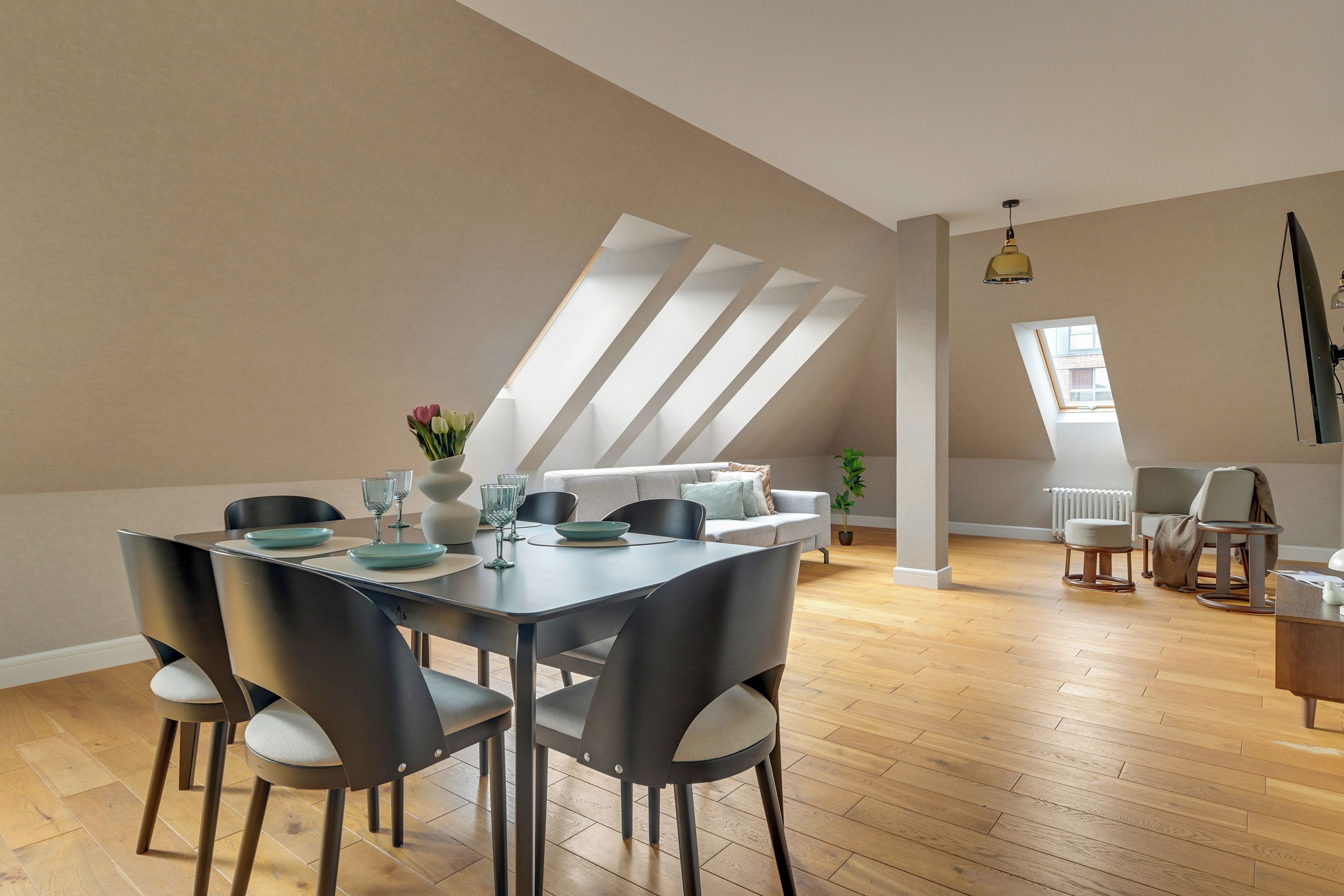 Un espace repas moderne avec une table dressée pour quatre personnes, entourée de chaises, dans une pièce dotée d’un plancher en bois et d’un plafond en pente.