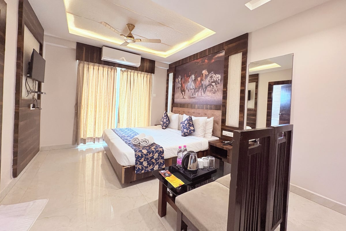 A hotel room with a bed, bedside table, ceiling fan, air conditioning unit, and a painting on the wall.