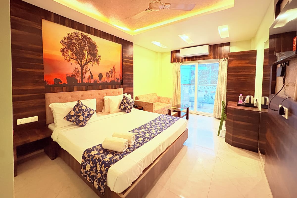 A bedroom with a large bed, a ceiling fan, a painting, a sofa, and a TV.