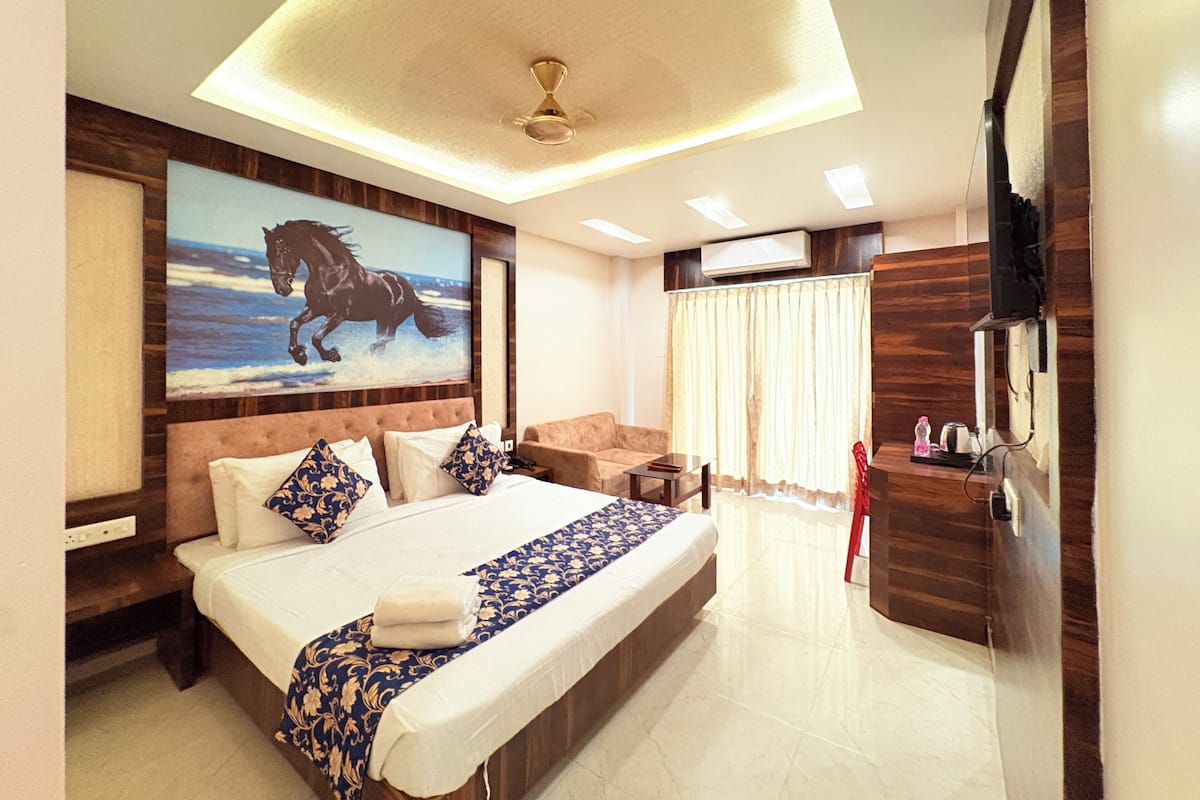 A hotel room with a bed, a mounted TV, a ceiling fan, a painting of a horse, and a window with curtains.