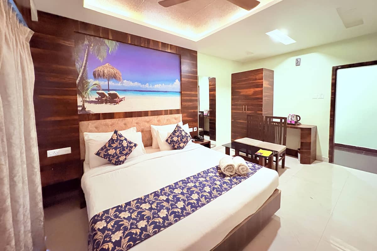 A hotel room with a bed, a desk, a chair, a ceiling fan, and a beach-themed wall art.