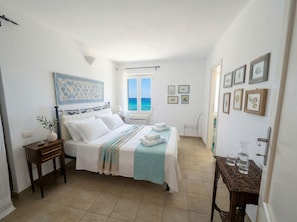 A bedroom with a bed, bedside table, window, and wall art. - ClickSardegna - Villa Horizon with Hot Tub and View over the Bay of Nymphs (Maristella)
