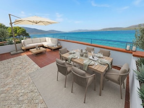 A terrace with a dining table set for six, a sofa, and a large umbrella. - ClickSardegna - Villa Horizon with Hot Tub and View over the Bay of Nymphs (Maristella)