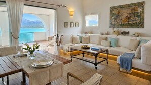 A living room with a sofa, a coffee table, a dining table set, and a view of the sea.