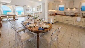 A modern kitchen with a dining area, large windows, and a view of the ocean.