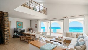 A spacious living area with a balcony overlooking the sea, a TV, and a fireplace.