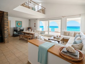 Un vaste espace de vie avec un balcon donnant sur la mer, une télévision et une cheminée.